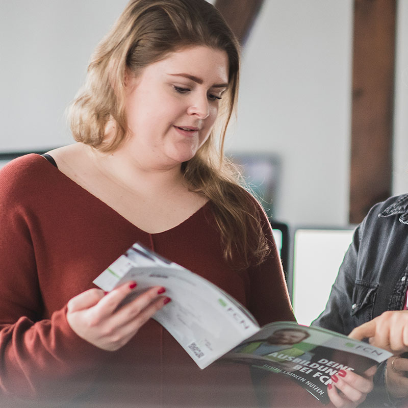 Frau Weber hält die FCN Azubi-Broschüre aufgeklappt in den Händen und betrachtet diese