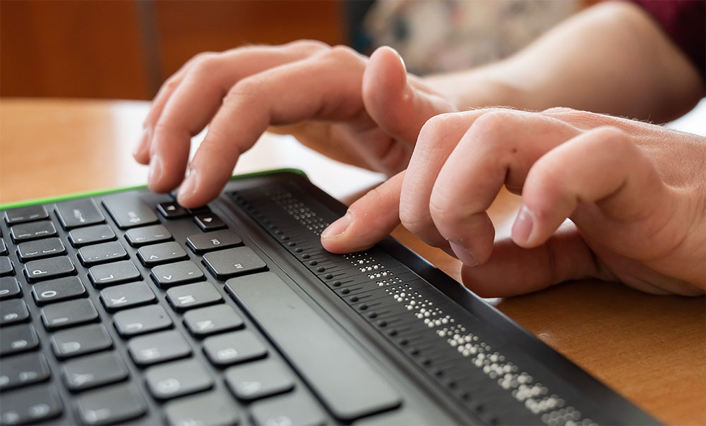 Nahaufnahme einer Blindentastatur, auf der eine Person mit beiden Händen tippt
